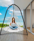 Woman sitting on Cozy Hanging Swing Nest Daybed White Saucer Style Hammock Chair indoors with ocean view, laptop in hand.