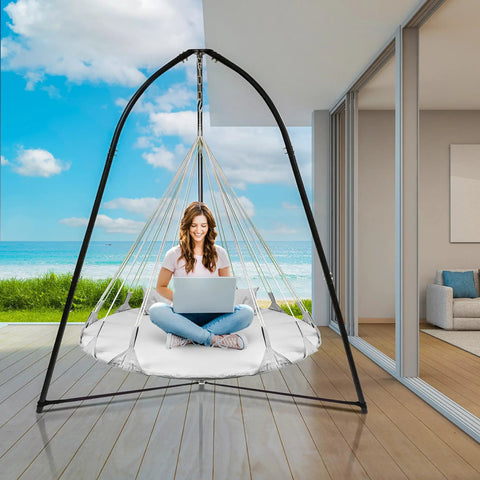 Woman sitting on Cozy Hanging Swing Nest Daybed White Saucer Style Hammock Chair indoors with ocean view, laptop in hand.