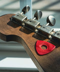 Red Axe Blade Medium Guitar Pick with Smooth Edge on guitar headstock, ergonomic grip, versatile 3 sided tip, flat 0.6mm and 2.0mm bevels