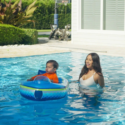 Toddler in motorized Remote Control Baby Pool Float With Enclosed Propeller Guard, adult in pool beside, sunny day