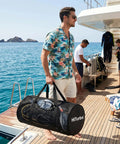 Man carrying 100L Duffel Scuba Bag For Diving And Watersports, Large Mesh Gear Tote with snorkeling equipment on yacht deck.