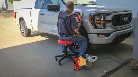 Rolling Shop Stool With Adjustable Height For Mechanics Padded Garage Seat With Smooth Rolling Wheels And ABEC Bearings Model 240250 Red in use by a mechanic working on a truck.