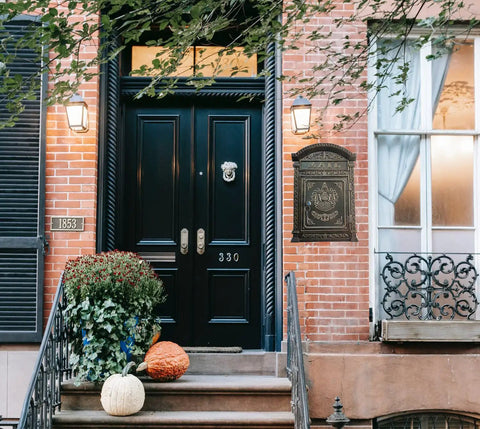 Outdoor Metal Wall Mounted Mailbox With Vintage Cast Iron Locking Look And Old School Charm on a brick wall near a black door.