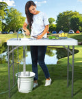 Person using 42.5 Inch Folding Fish Cleaning Table With Sink And Hose Hookup Portable Outdoor Fishing Station at park campsite.