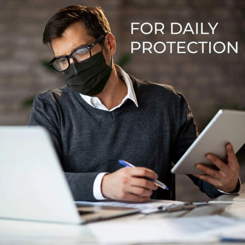 Man wearing IMask Premium ASTM Level 3 Face Mask Black Pack Of 50 With Soft Multilayer Nonwoven Fabric and working at a desk.