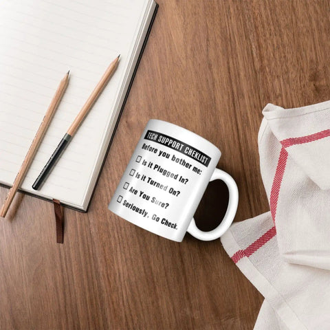 Funny Tech Support Checklist Coffee Mug for Help Desk Heroes on wooden table near pencils and notebook, 11oz ceramic cup
