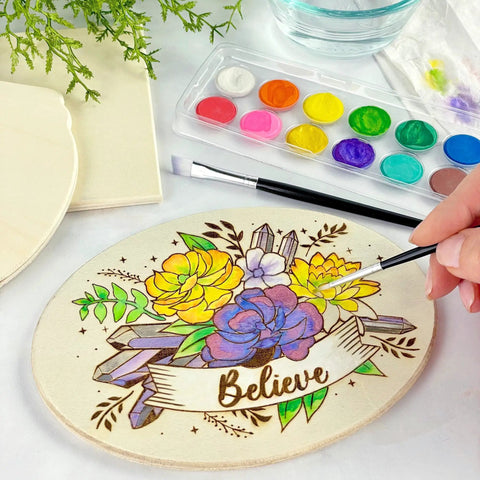 Person painting floral design on plaque from Starter Wood Burning Kit With Burner Pen, 5 Interchangeable Tips, 48-Piece Deluxe Pyrography Set
