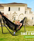 Man relaxing on a black Beefy Heavy Duty Steel Hammock Stand For 9 To 14 Foot Hammocks With 550 Lb Capacity, Portable Frame, Dual Bar Design in backyard.