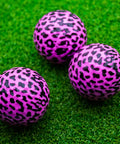 Three pink leopard print novelty golf balls on green grass, part of 12 pack with bold 360 degree leopard design, gift for golfers.