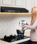 Woman cooking under 36 Inch Under Cabinet Range Hood With 900 CFM Dual Motors Black Kitchen Vent Hood For Real Heavy Duty Cooking