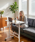 Person using Adjustable Standing Desk On Wheels For Treadmills And Home Offices Portable Laptop Workstation, white, in living room.