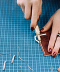 Person using 7 In 1 Pro Grade Leather Groover Tool And Cutting Knife Set for DIY leathercraft on a blue grid mat