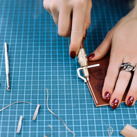 Person using 7 In 1 Pro Grade Leather Groover Tool And Cutting Knife Set for DIY leathercraft on a blue grid mat