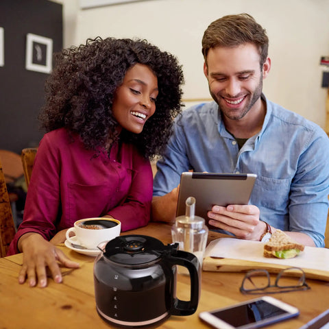 Man and woman at table with a 12 Cup Drip Coffee Maker With Auto Off And Reusable Filter, Borosilicate Glass Carafe, Anti Drip Water Window in black.