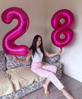 Woman holding pink foil number 2 and Hot Pink Number 8 Balloon 40 Inch Giant Foil Balloon For 8th Birthday Party Decor Epic Photo Backdrop Prop Large 8 Balloon For Party Supplies Bold Birthday Decor That Pops And Stays Put on sofa