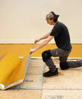 Man installing Premium Flooring Underlayment Roll 100 Sq Ft 2Mm Thick with pre-taped sides on floor.