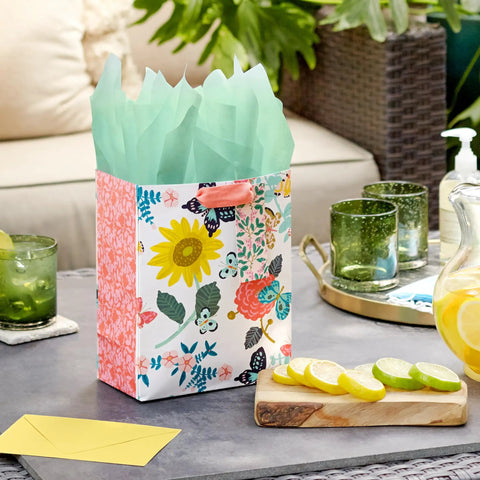 Nine Inch Medium Gift Bag With Tissue Paper Bright Flower Designs For Valentine Day Easter Birthdays Bridal Showers Weddings Baby Showers And Mothers Day A Cute Floral Gift Bag For Any Special Occasion on a patio table.