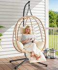 Woman relaxing in Hanging Egg Chair With Five Level Adjustable Footrest And Stand, Wicker Rattan, on a patio.