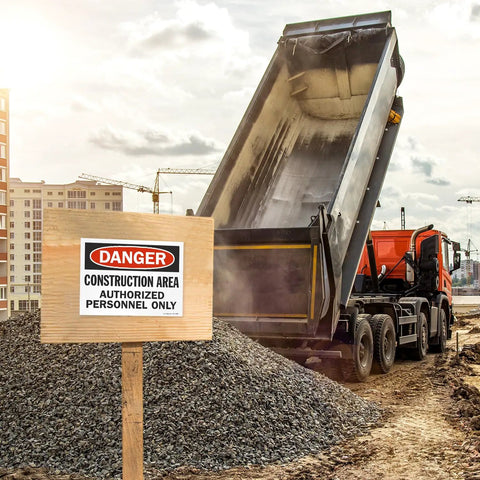 Danger Construction Area Authorized Personnel Only OSHA sign in front of active construction site with dump truck and gravel pile.