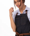 Unisex Memphis Bib Apron In Indigo Blue With Adjustable Neck Buckle And Waist Ties worn by a person, showing front pockets.