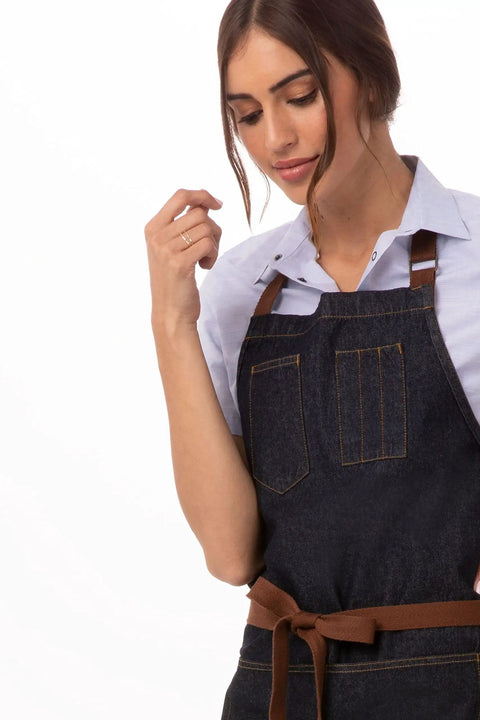 Unisex Memphis Bib Apron In Indigo Blue With Adjustable Neck Buckle And Waist Ties worn by a person, showing front pockets.