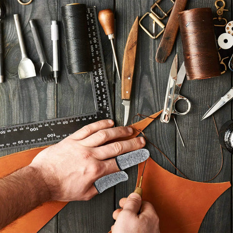 Crafting with 20 Piece Cut Resistant Finger Cots And Finger Sleeves Reusable Thumb Protectors, shown handling leather tools on a table.