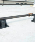 Rooftop pipe stand with two black recycled-plastic saddles, pipe resting across them on a concrete roof