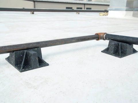 Rooftop pipe stand with two black recycled-plastic saddles, pipe resting across them on a concrete roof