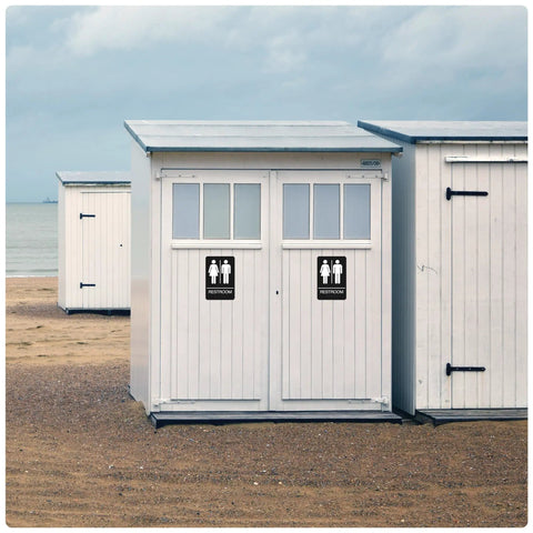 Beachside restroom cabin with male and female signs on white doors with modern design.