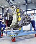 Two technicians working on an aircraft engine mounted on a cart with swivel casters in an industrial setting.