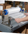 Manual Stretch Film Dispenser For Cargo Packaging And Wrapping Supplies With Durable Metal Plastic Assembly, Lightweight Design, Easy To Use Roll Holder, Reduces Collision Damage, Protects Goods During Shipping And Storage on a workbench with bubble wrap