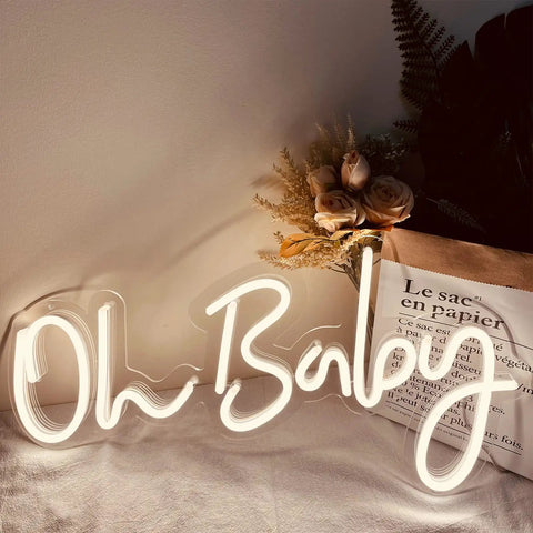 Oh Baby Neon Sign White LED Wall Decor With Dimmable Brightness And Plug In Power Adapter, illuminated on a wall near flowers.