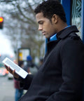Sleek White Second Gen Ereader Features A Sharp Six Inch Screen And Free 3G Wireless To Pull Down Books Anywhere, held by man in black coat.