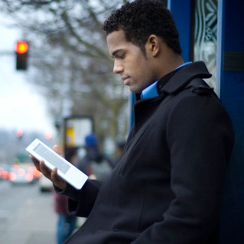 Sleek White Second Gen Ereader Features A Sharp Six Inch Screen And Free 3G Wireless To Pull Down Books Anywhere, held by man in black coat.