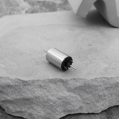 Close-up of a Two Pack 12V DC Mini Motors 13477RPM Micro 1015D Motors on a stone surface, showing compact design and metal body.