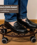 Person standing on Three Pack Heavy Duty Metal Plant Caddies With Wheels 13.5 Inch rolling plant stand dolly, showcasing strength.