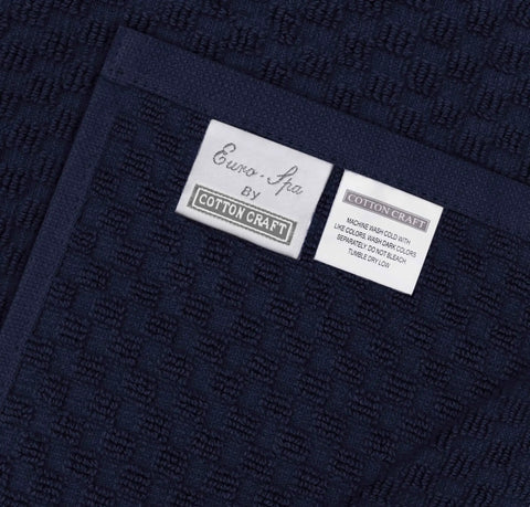 Close-up of navy blue waffle weave cotton fabric with brand labels for Two Pack Navy Blue Pool Lounge Chair Covers With Waffle Weave Cotton Terry Towels, Oversized 32 Inch Wide By 82 Inch Long Chaise Covers With A 7 Inch Pocket, Absorbent Beach Chair Towel Set.