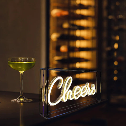 Plug And Play USB LED Lightbox Cheers Sign With 3D Neon Glow For Bar And Home Decor on a table next to a cocktail glass.