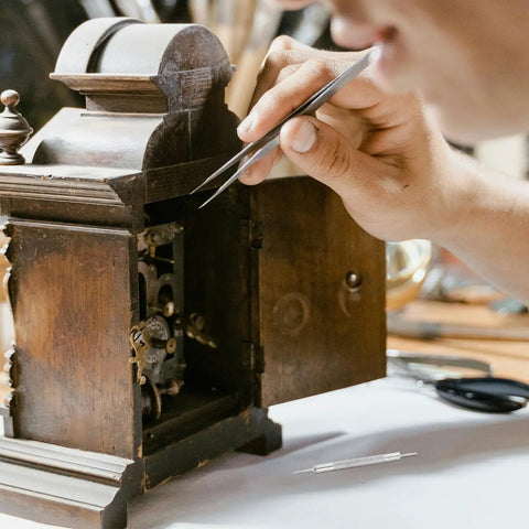 Person using tweezers to repair vintage clock with Stainless Steel Watch Band Pins And Spring Bars Replacement Kit 110pcs tool on table.