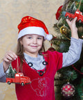 Child holding Three Pack Totally Vintage Red Truck Christmas Ornaments With Mini Christmas Trees near decorated tree