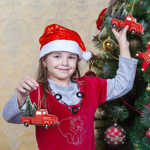 Child holding Three Pack Totally Vintage Red Truck Christmas Ornaments With Mini Christmas Trees near decorated tree