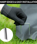 Gloved hand installing Heavy Duty 6 Inch U-Shaped Landscape Staples Set, 120 Pack, 11 Gauge Galvanized Steel Garden Stakes for sod and weed barrier.