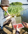 Angler with open box of 50 Pcs 1-1/2 Inch Sinker Slides With Metal Snaps For Catfishing on dock by lake.