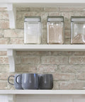 Denver Brick White Washed Peel And Stick Wallpaper behind kitchen shelves with jars and mugs