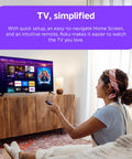 Woman using remote with 55 Inch QLED Smart TV displaying Roku interface in cozy living room setting.