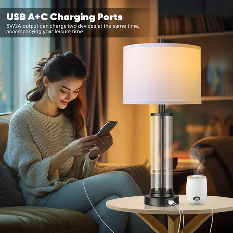 Touch Control Table Lamps Set Of 2 With USB Ports And 3 Way Dimmable Bedside Lighting For Living Room And Bedroom Modern Black Nightstand Lamps With 2 LED Bulbs, showing one lamp next to a woman using a smartphone.