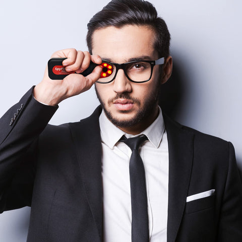 Man using Hidden Camera Detector And Spy Camera Finder For Hotels And Travel against glasses, LED lights on, portable use
