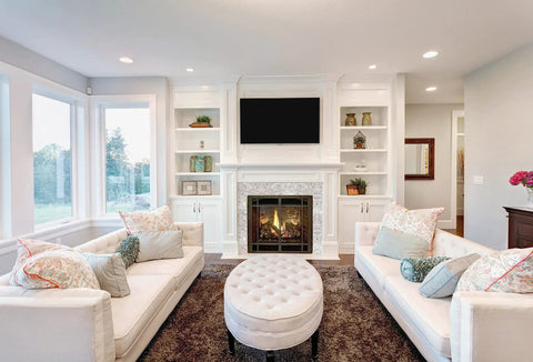 Elegant living room with white sofas, large windows, and a fireplace with built-in shelves displaying decor.
