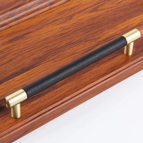 Brushed Satin Gold Bar Cabinet Handle With Black Leather Upholstery 8.5 Inch Overall Length, mounted on wooden surface
