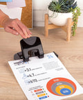 Built Different Two Hole Punch Crushes Twenty Sheets Like Nothing Else With Smart Touch Low Effort Grip And Tight Accuracy Alignment Track For Quick Paper Organizing Jobs In Sleek Black Gray being used on a document.
